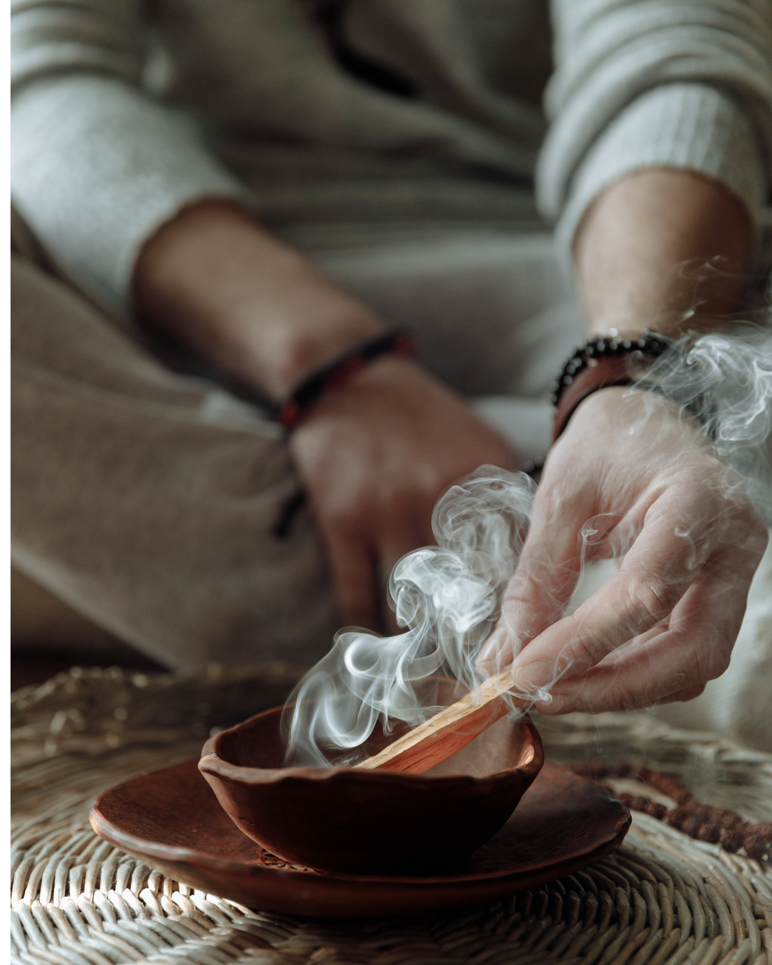 A hand holding a burning Palo Santo stick with smoke swirling — perfect for intention setting and clearing negative energy.