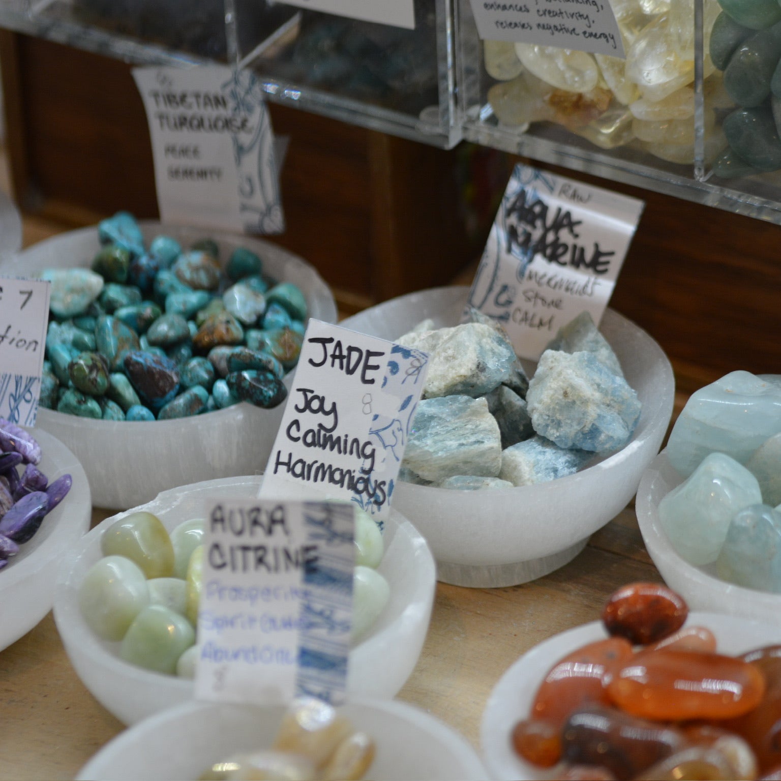 Display of various types of stones in bowls with descriptive labels on a wooden surface.