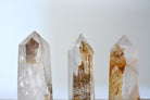 Side view of a polished Golden Healer Quartz tower with natural dendritic inclusions and glowing golden hues — ideal for altar or meditation use.