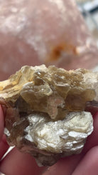 A close-up of a person's hand holding a rough, crystalline mineral specimen with layered translucent yellow-brown and clear sparkly facets. 