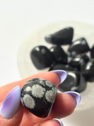 Snowflake Obsidian tumbled stone resting in a hand, showing size and natural pattern — a grounding crystal for protection and emotional clarity.