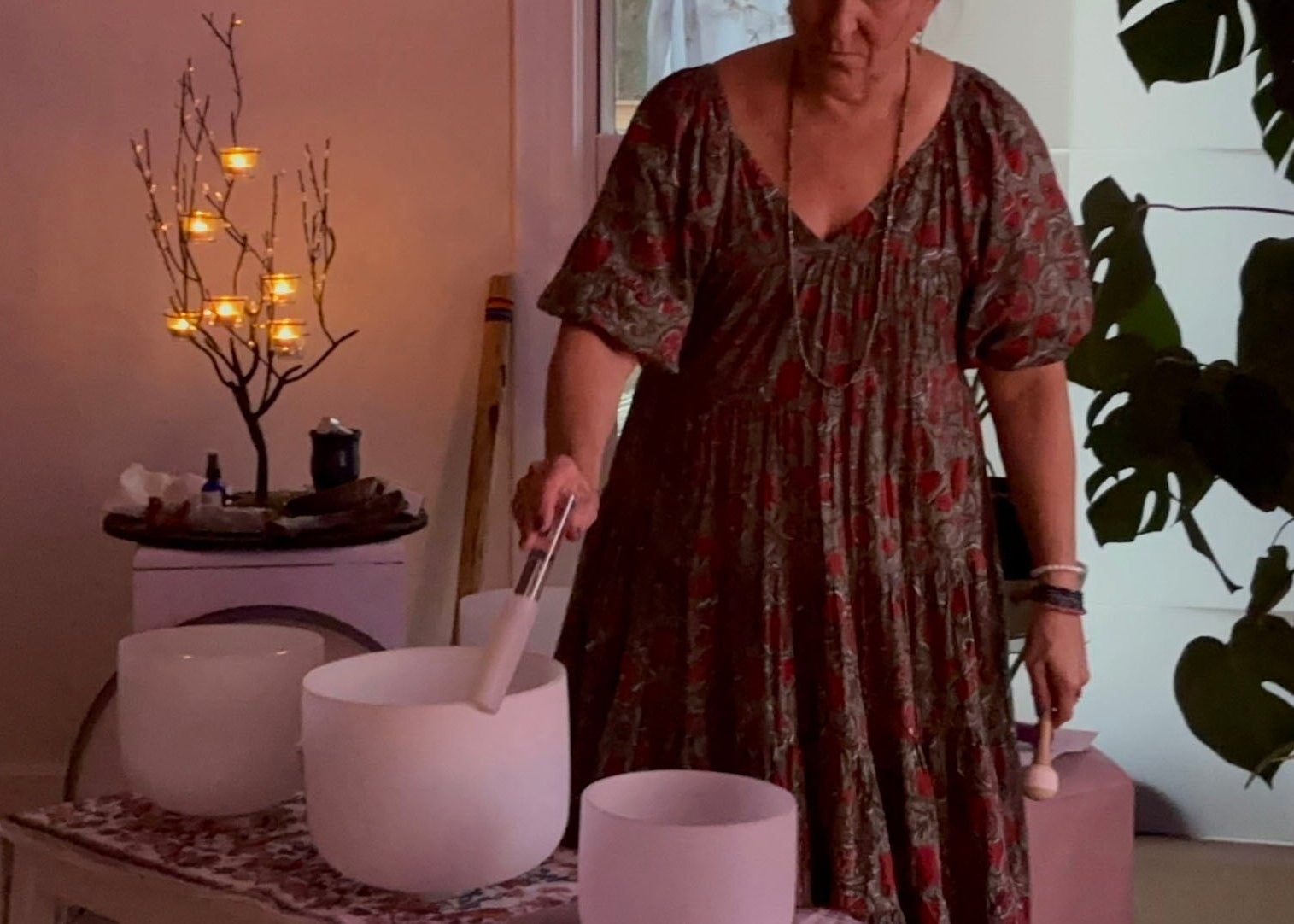 Woman in a patterned dress standing in a room with white bowls and a plant.